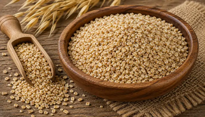 A dark wooden bowl overflowing with raw, organic steel-cut oats, with a matching wooden scoop spilling grains onto a rustic burlap cloth and wooden table background