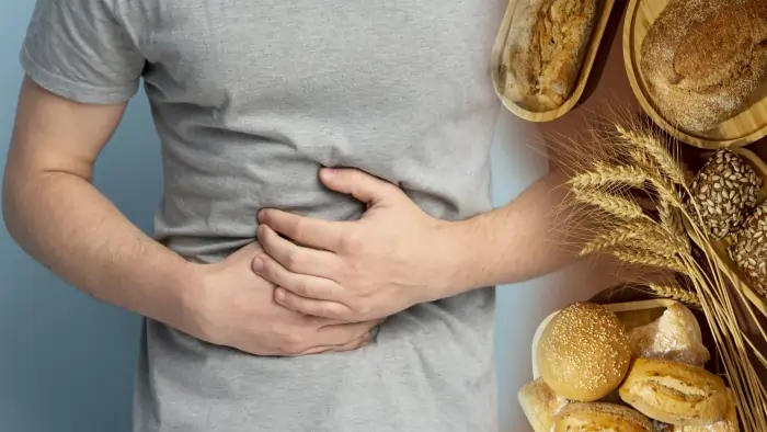 Person experiencing stomach pain beside wheat-based foods, representing celiac disease and gluten intolerance symptoms caused by gluten-containing products.